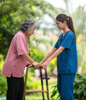 Caregiver supporting senior woman with walking assistance outdoors